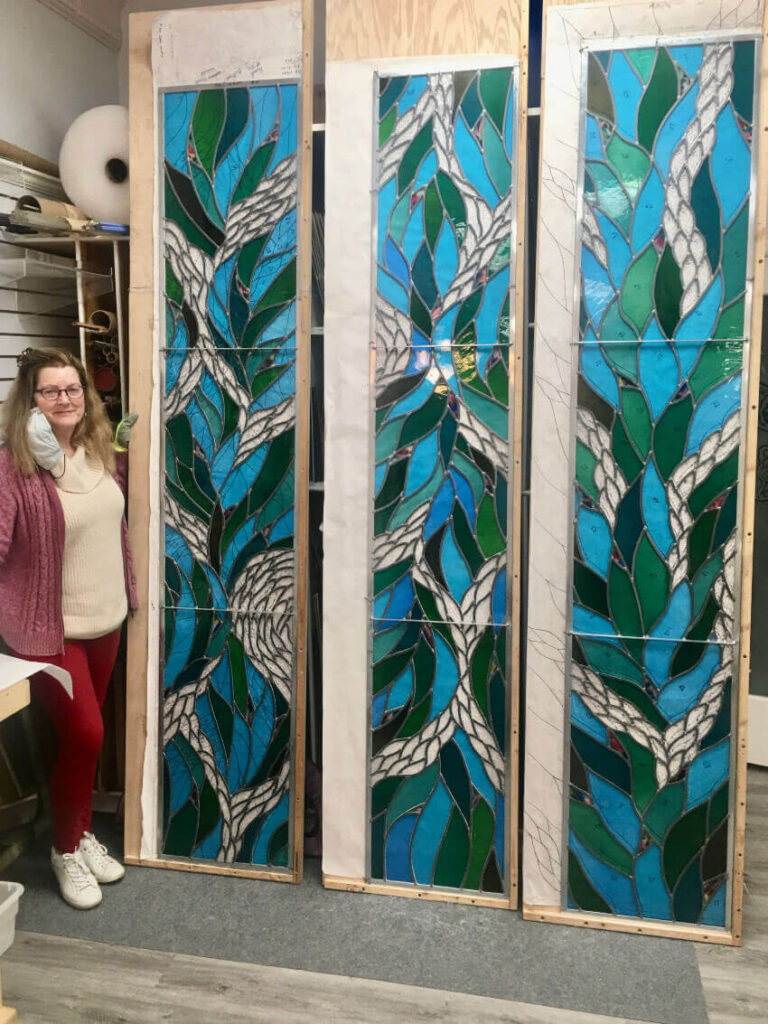 Michaele Rose standing next to 4 upright stained glass panels